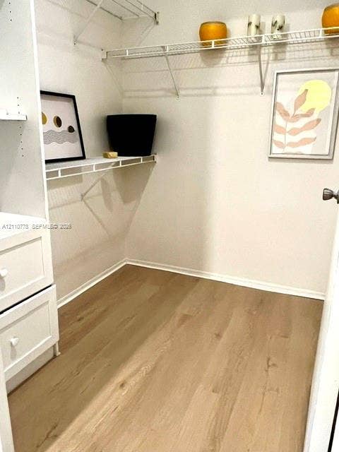 Walk-in closet featuring white built-in drawer cabinetry, wood-finish flooring, and tiered wire shelving