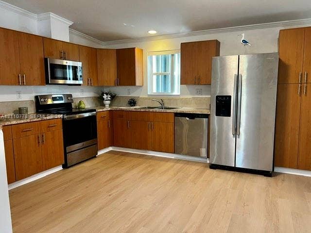 Kitchen featuring wood-finish cabinetry, stone-style countertops, stainless steel appliances, and light-tone wood-finish flooring