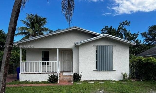 Stucco exterior featuring a covered front porch with white railing, a gabled roofline, and established landscaping