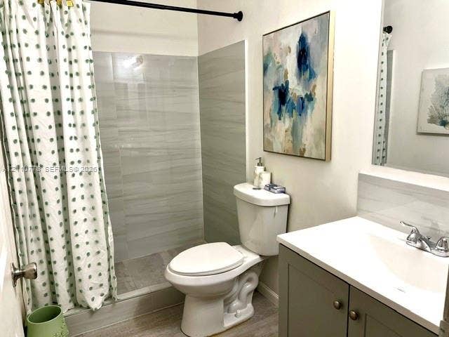 Bathroom featuring neutral-toned tile shower surround, grey vanity cabinet with integrated white countertop, and brushed metallic hardware