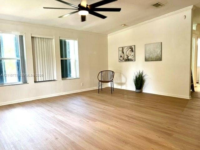 Living area featuring wood-finish flooring, multi-pane windows, crown molding, and a matte black ceiling fan