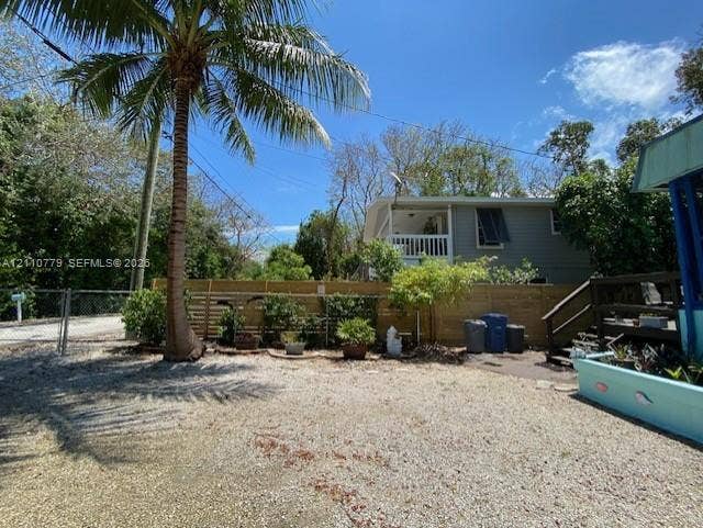 Gravel grounds featuring a privacy fence, mature palm tree, and exterior staircase