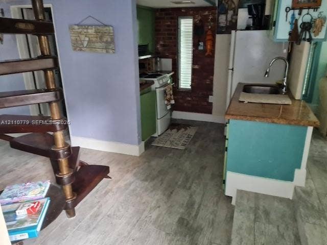 Spiral wooden staircase with turned spindles, exposed brick accent wall, wood-finish flooring, and kitchen island featuring a stainless steel undermount sink with a gooseneck faucet