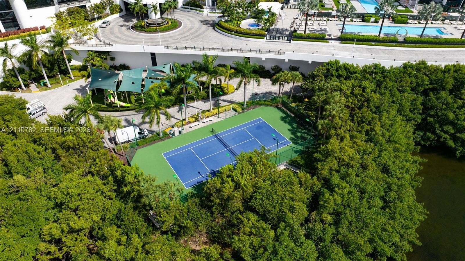 Tennis court with perimeter fencing, outdoor swimming pool, circular paved motor court, and canopy-covered recreation area