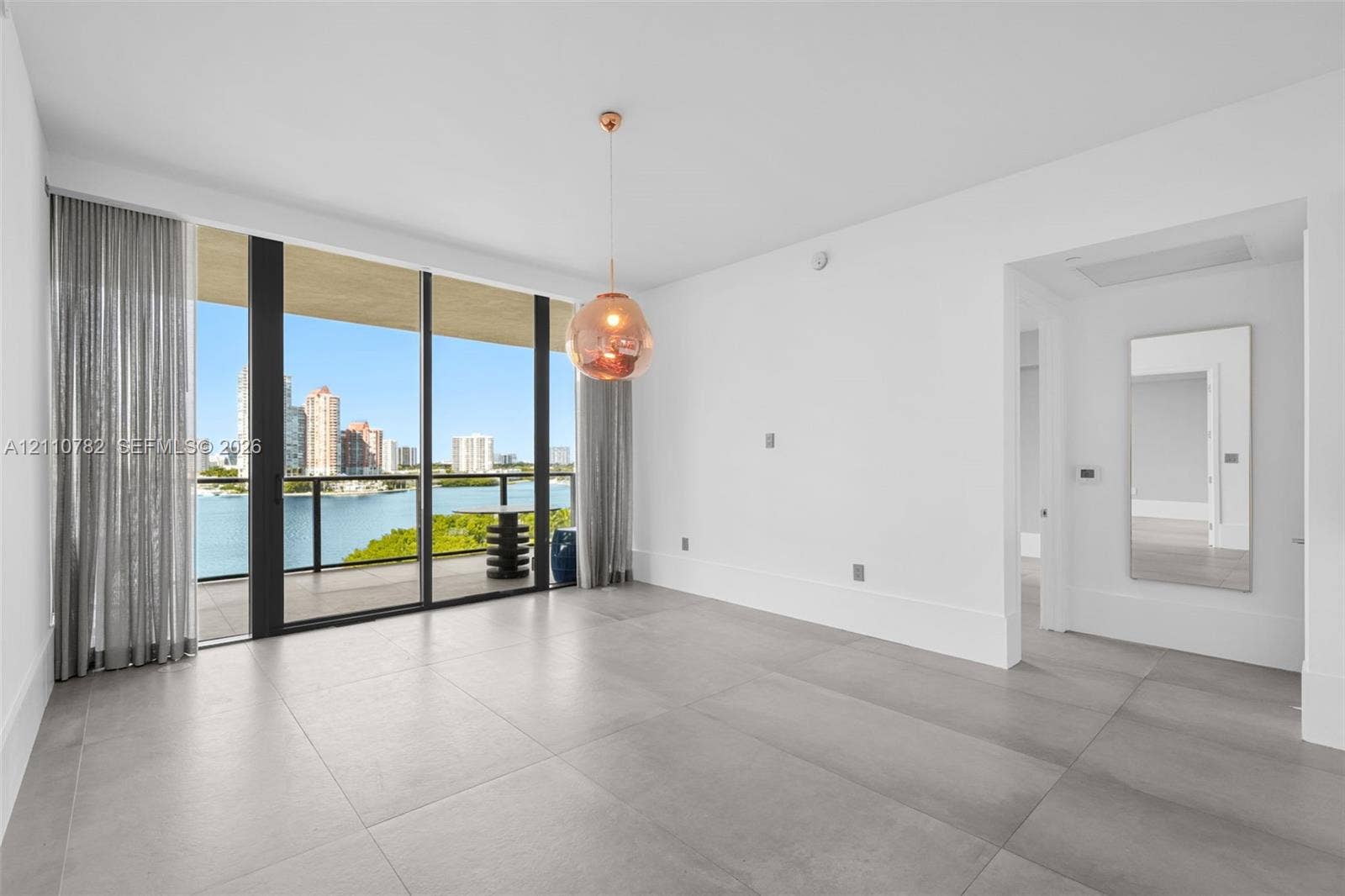 Floor-to-ceiling sliding glass doors, private balcony, large-format tile flooring, metallic pendant lighting, and wall-mounted mirror
