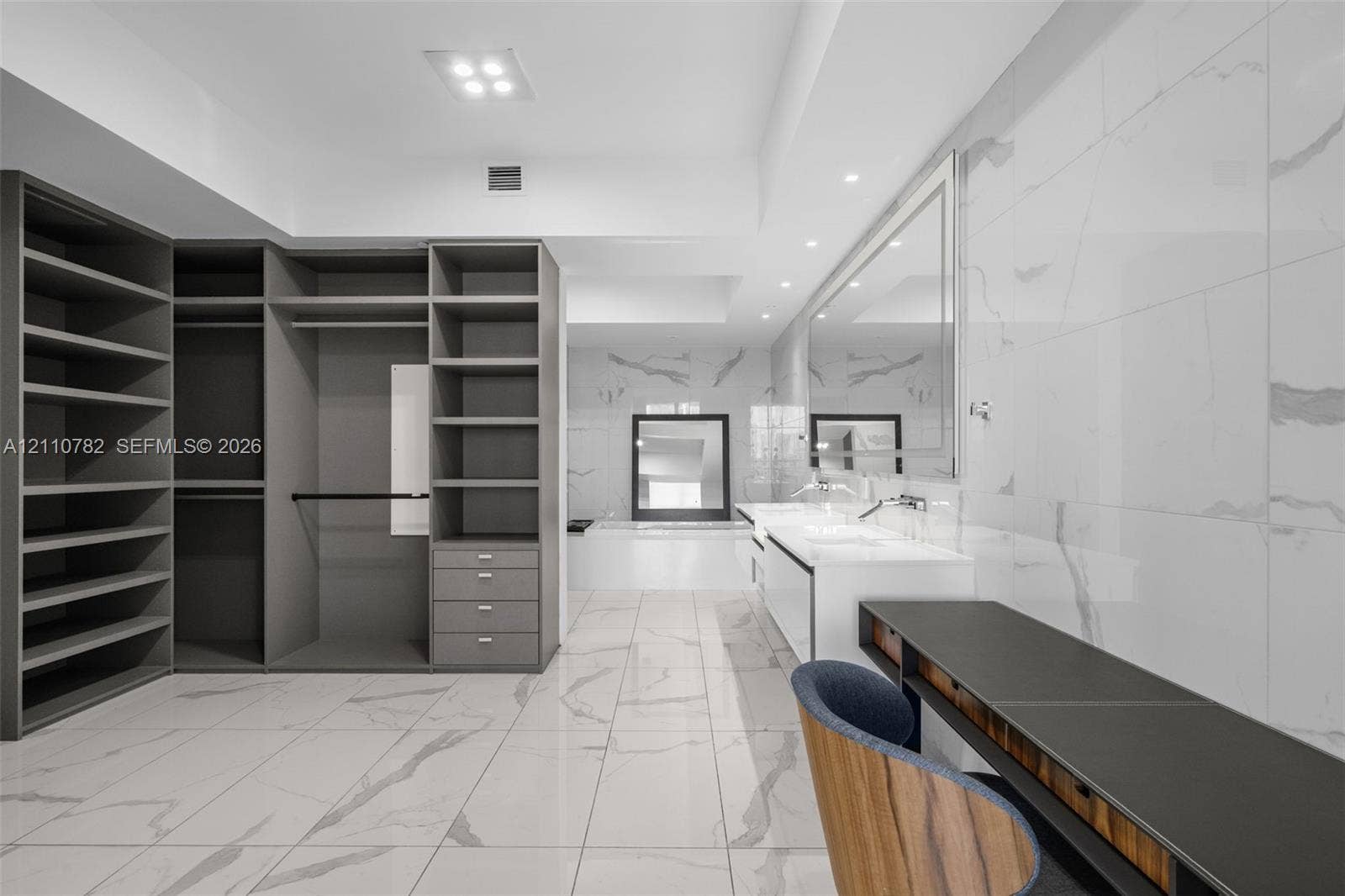 Custom built-in storage system with grey cabinetry, large-format tiled flooring, wall-to-wall vanity with dual sinks, and full-height tiled wall detailing