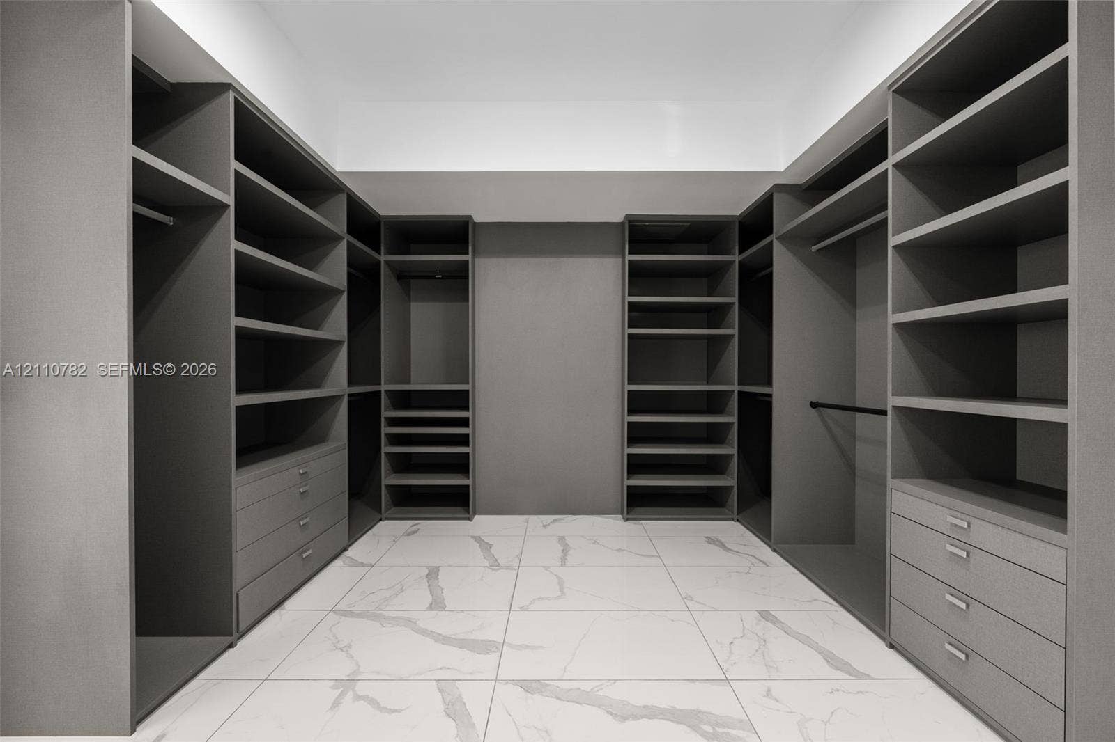 Walk-in closet featuring extensive built-in shelving, integrated hanging rods, custom cabinetry with pull-out drawers, and large-format tile flooring