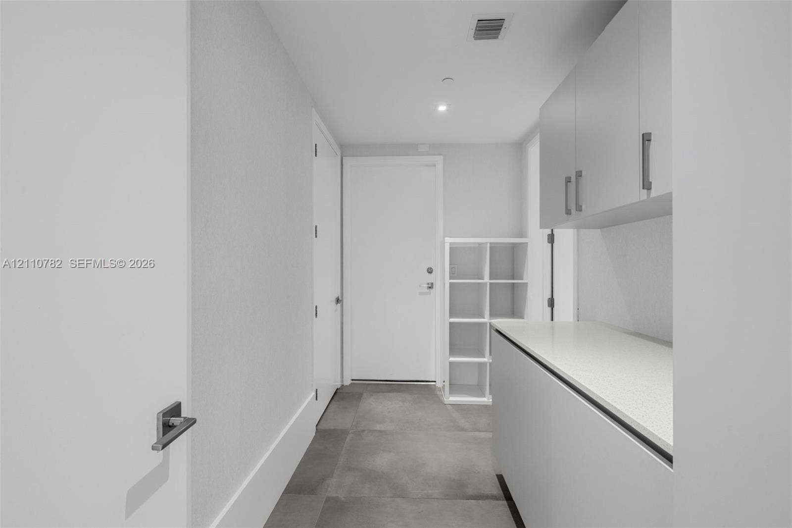 Utility area featuring large-format tile flooring, built-in light-tone cabinetry, stone-composite countertops, and integrated storage shelving