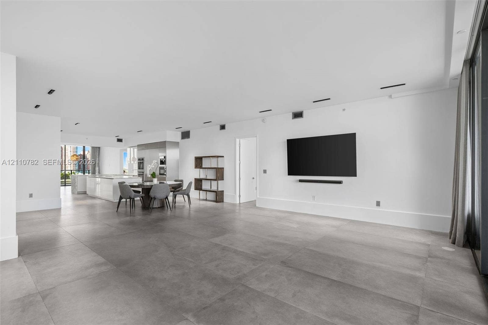 Open concept interior featuring large-format grey tile flooring, recessed ceiling lighting, and a neutral white color palette