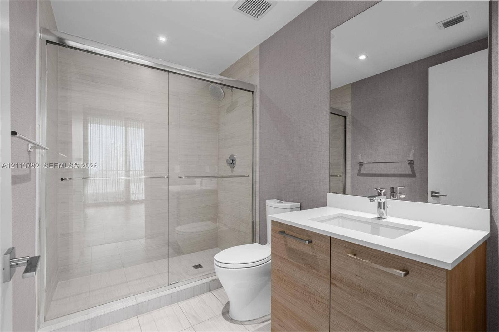 Bathroom featuring a glass-enclosed walk-in shower with tile surround, vanity with a light-tone wood finish, solid-surface countertop, and an integrated rectangular basin