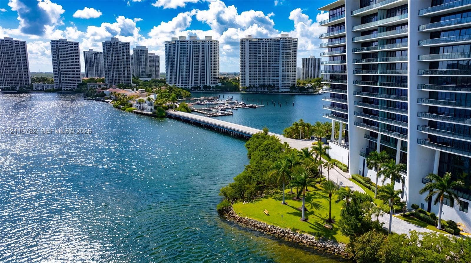 High-rise residential exterior featuring stacked private balconies, waterfront grounds with palm trees, and direct access to a private dock facility