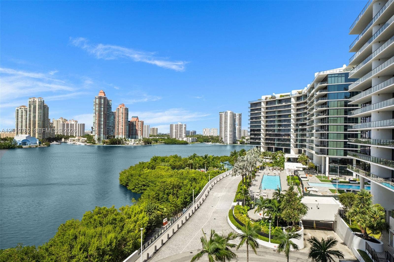 High-rise architecture with expansive glass-railed balconies, waterfront location, multi-level swimming pools, and landscaped grounds with mature palms