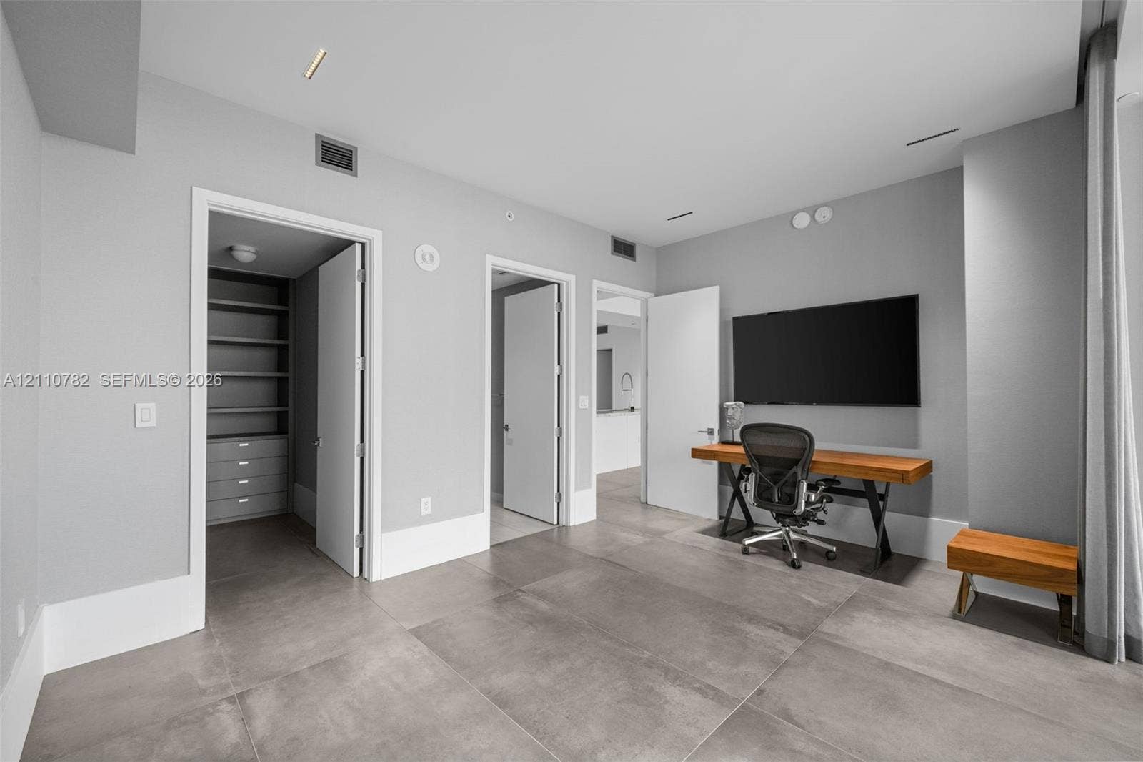 Large-format tile flooring, recessed ceiling lighting, and a walk-in closet featuring built-in shelving and integrated cabinetry