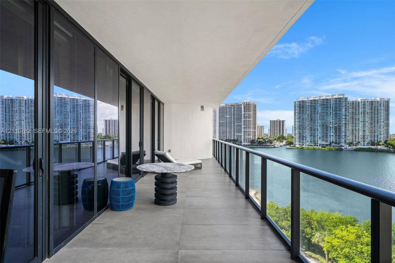 Covered balcony featuring large-format stone-finish tiling, full-height glass sliding doors, and a sleek metal railing with glass panels