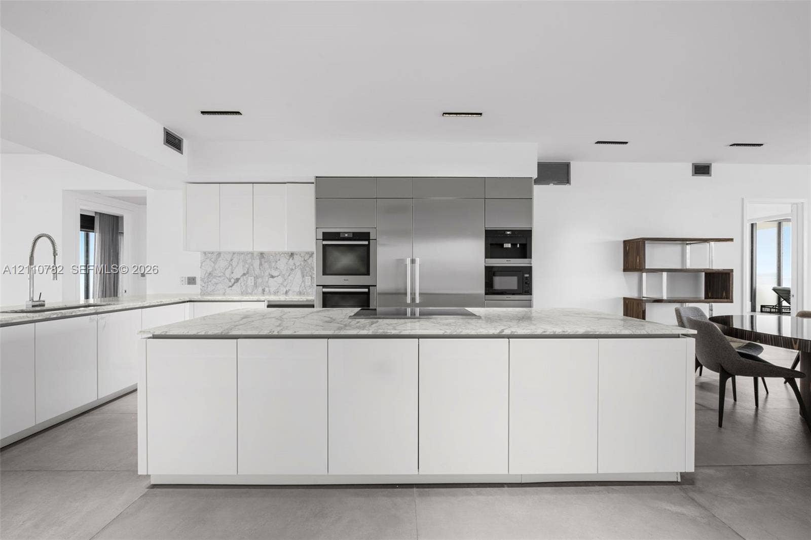 Contemporary kitchen featuring an expansive center island with stone surfacing, stainless steel built-in appliances, flat-panel cabinetry, a stone backsplash, and large-format floor tiling