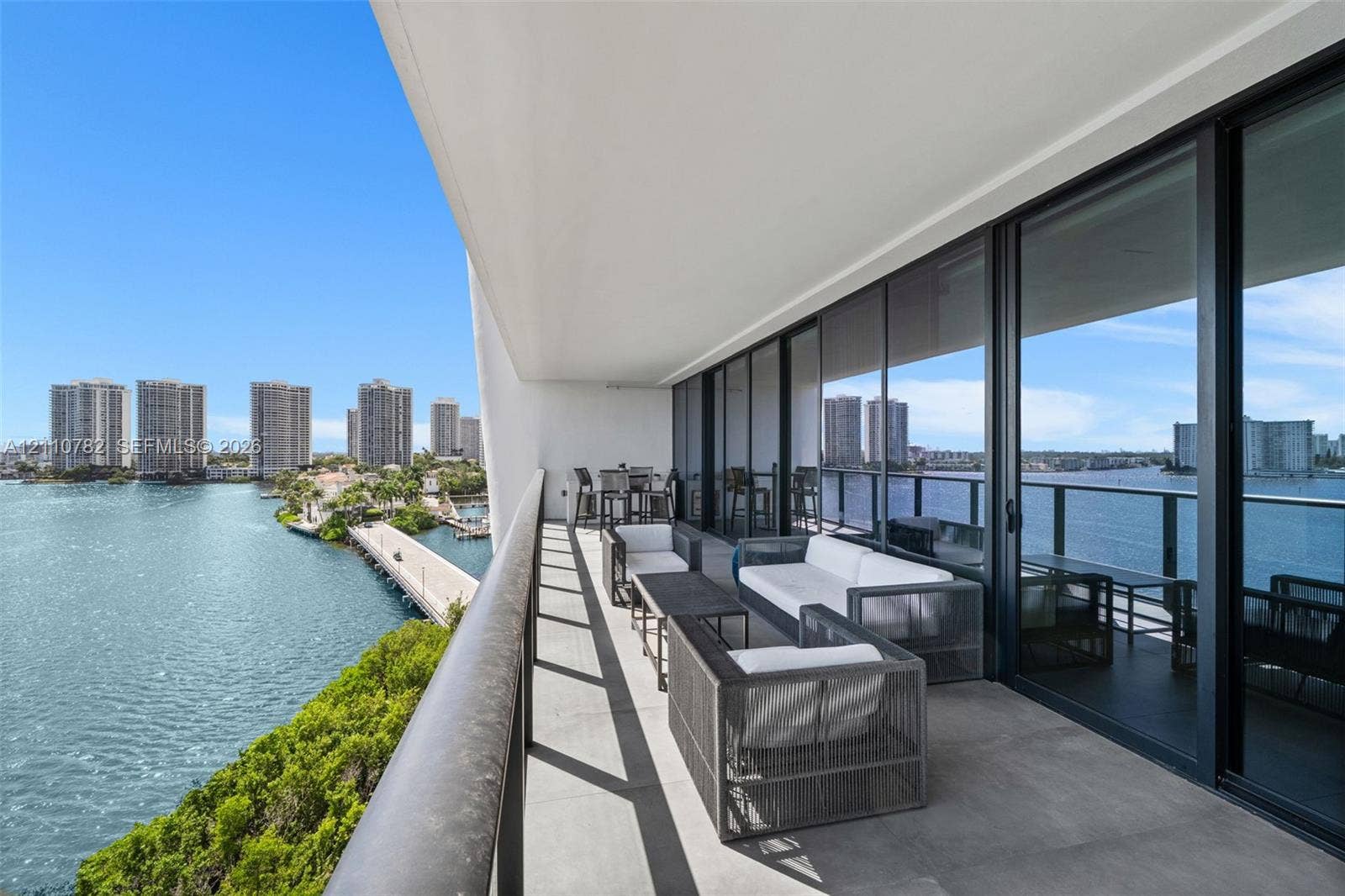 Expansive covered balcony featuring glass panel railings, tiled flooring, and floor-to-ceiling sliding glass wall panels overlooking the waterfront