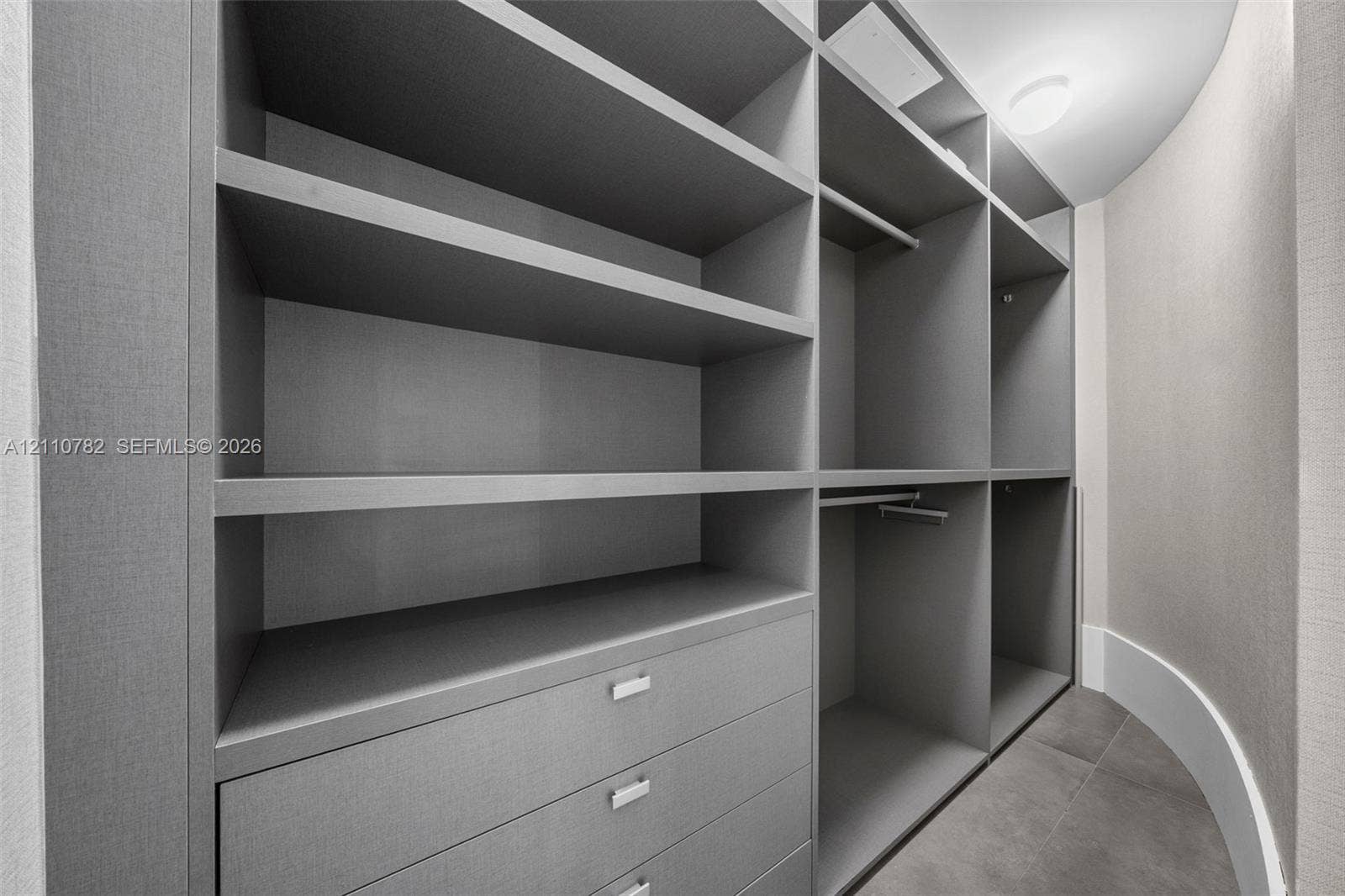 Custom organizational system featuring floor-to-ceiling cabinetry, integrated shelving, hanging rods, and built-in drawers with metallic hardware, set against tiled flooring