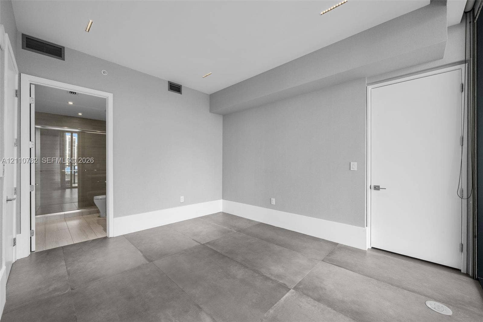 Interior room featuring large-format grey tile flooring, neutral wall tones, recessed linear ceiling lighting, and solid-core interior doors