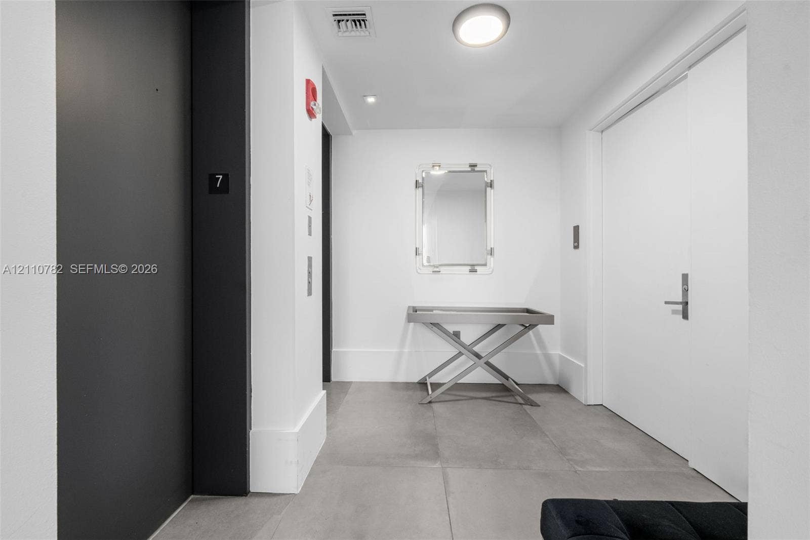 Entry foyer featuring large-format grey tile flooring, minimalist white walls, recessed ceiling lighting, and a matte black elevator entrance