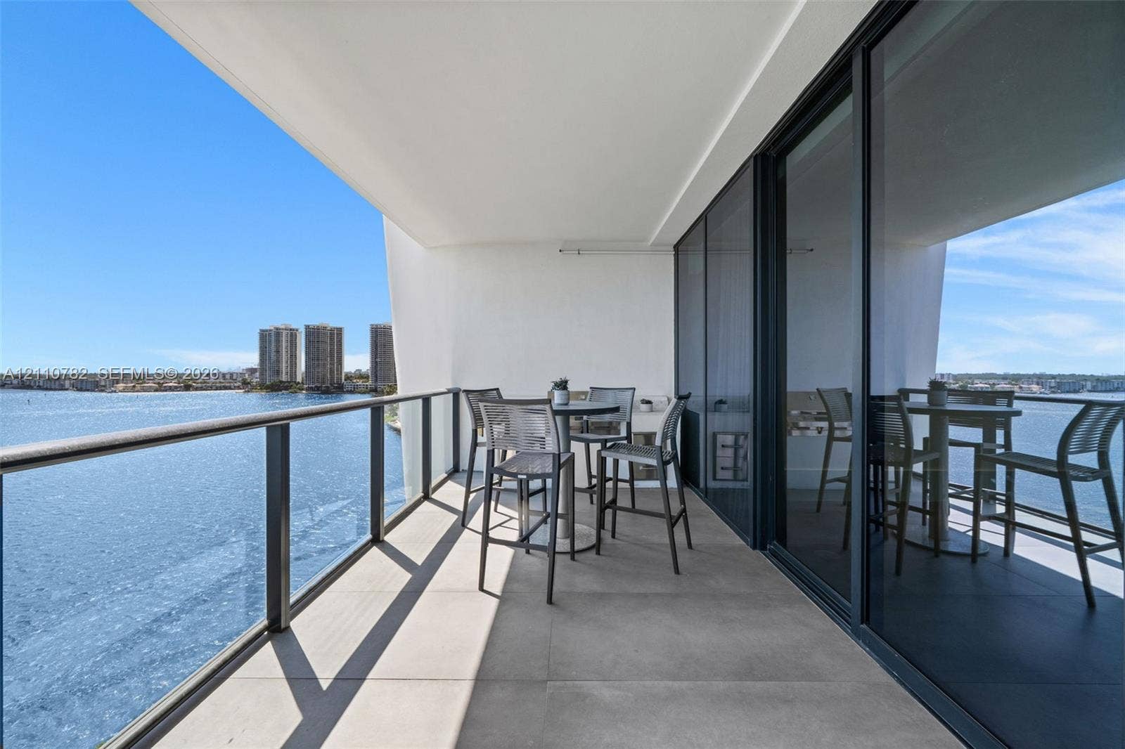 Covered balcony featuring large-format stone tile flooring, a metal and glass railing system, and full-height sliding glass doors