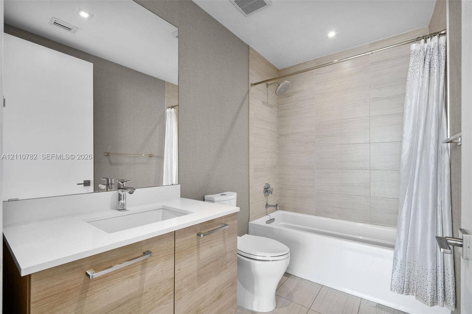 Bathroom featuring a vanity with a light wood-finish cabinet and solid-surface countertop, a rectangular undermount sink, recessed ceiling lighting, and a bathtub with a tiled surround