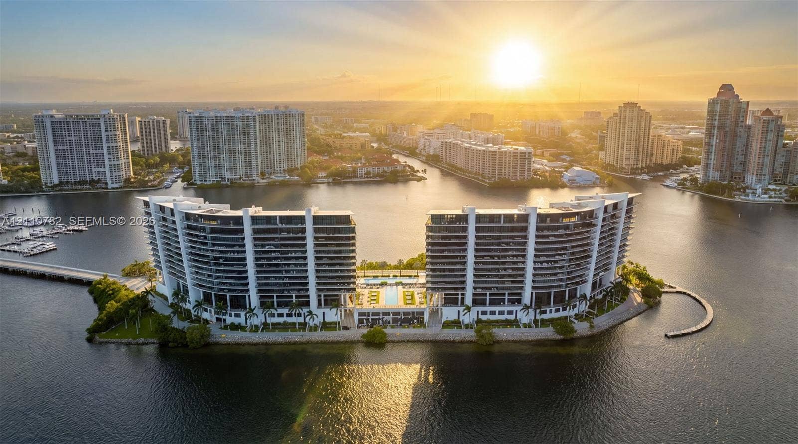 Waterfront high-rise complex situated on a peninsula, featuring multiple balconies, a swimming pool, and hardscaped recreational grounds