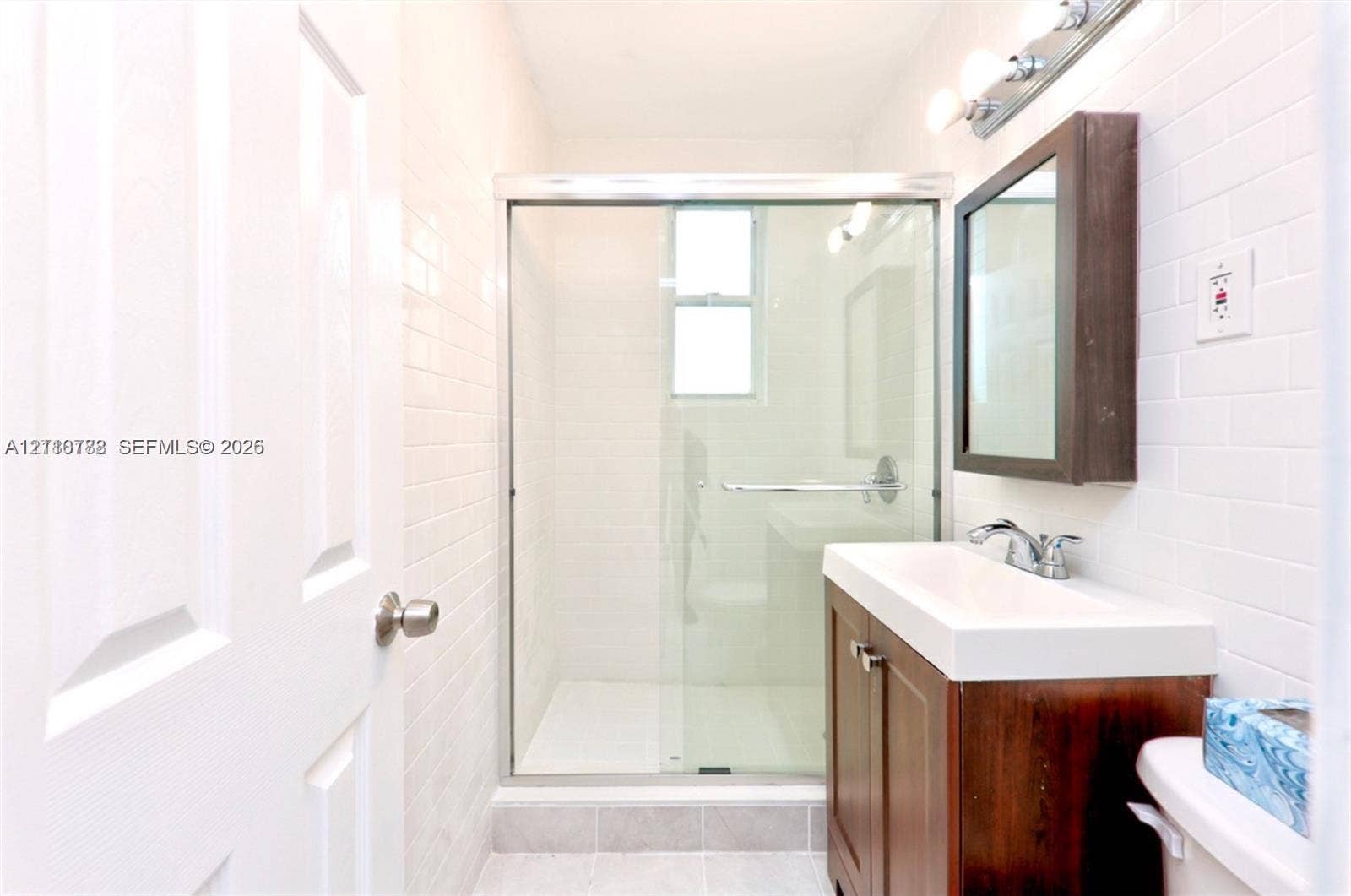 3710 Collins Avenue, #N-202, Miami Beach, FL 33140 Walk-in glass-enclosed shower featuring white subway-style wall tile, dark wood-finish vanity with a rectangular sink, chrome fixtures, and a wall-mounted medicine cabinet