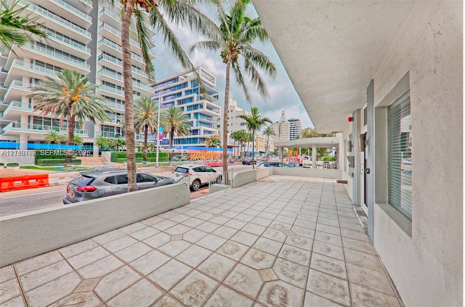 3710 Collins Avenue, #N-202, Miami Beach, FL 33140 Covered exterior terrace featuring geometric tile flooring, concrete perimeter wall, and built-in glass paneled entry
