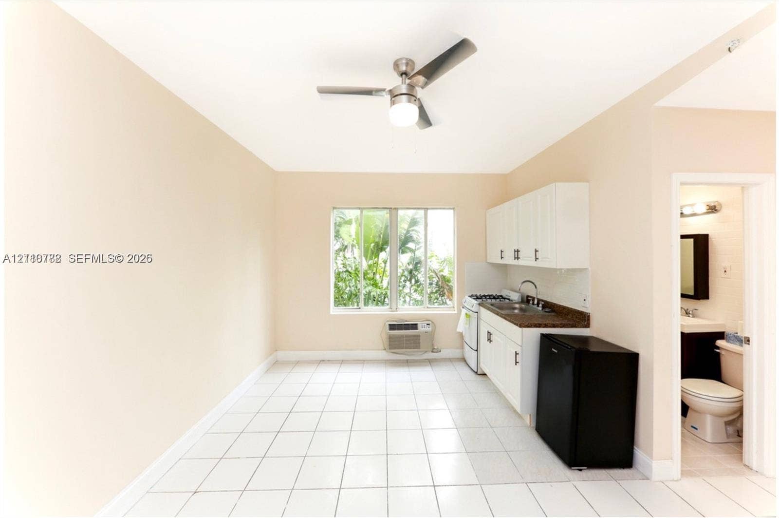 3710 Collins Avenue, #N-202, Miami Beach, FL 33140 Kitchenette featuring white cabinetry, dark stone-finish countertops, stainless steel sink with pull-down faucet, and white ceramic tile flooring, complemented by a ceiling fan