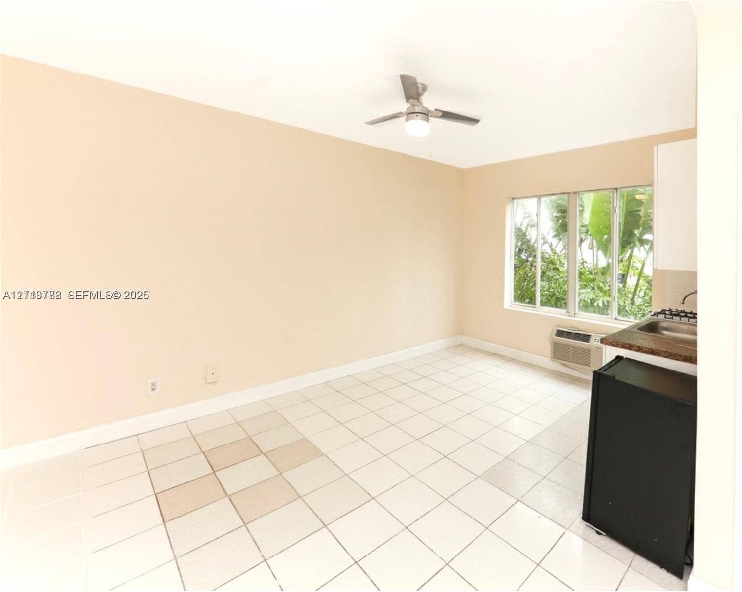 3710 Collins Avenue, #N-202, Miami Beach, FL 33140 Interior space featuring neutral wall paint, white tile flooring, a ceiling fan with an integrated light fixture, large multi-pane windows, and a built-in kitchenette area with a sink