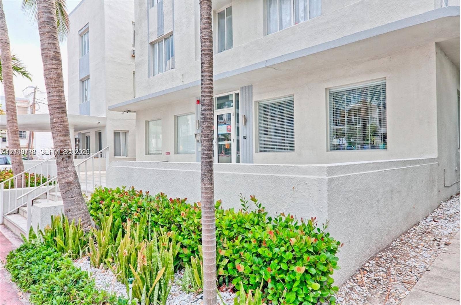 3710 Collins Avenue, #N-202, Miami Beach, FL 33140 Mid-century modern exterior featuring a smooth stucco facade, multi-pane windows, a recessed glass-paned entrance, and structured tropical landscaping