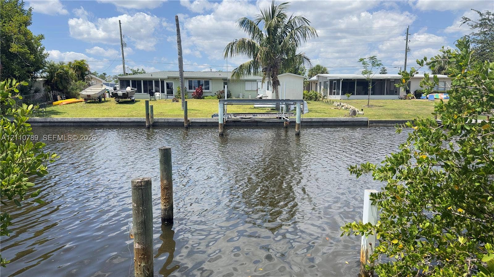 Waterfront property featuring a private boat lift, concrete seawall, expansive lawn, and mature palm tree