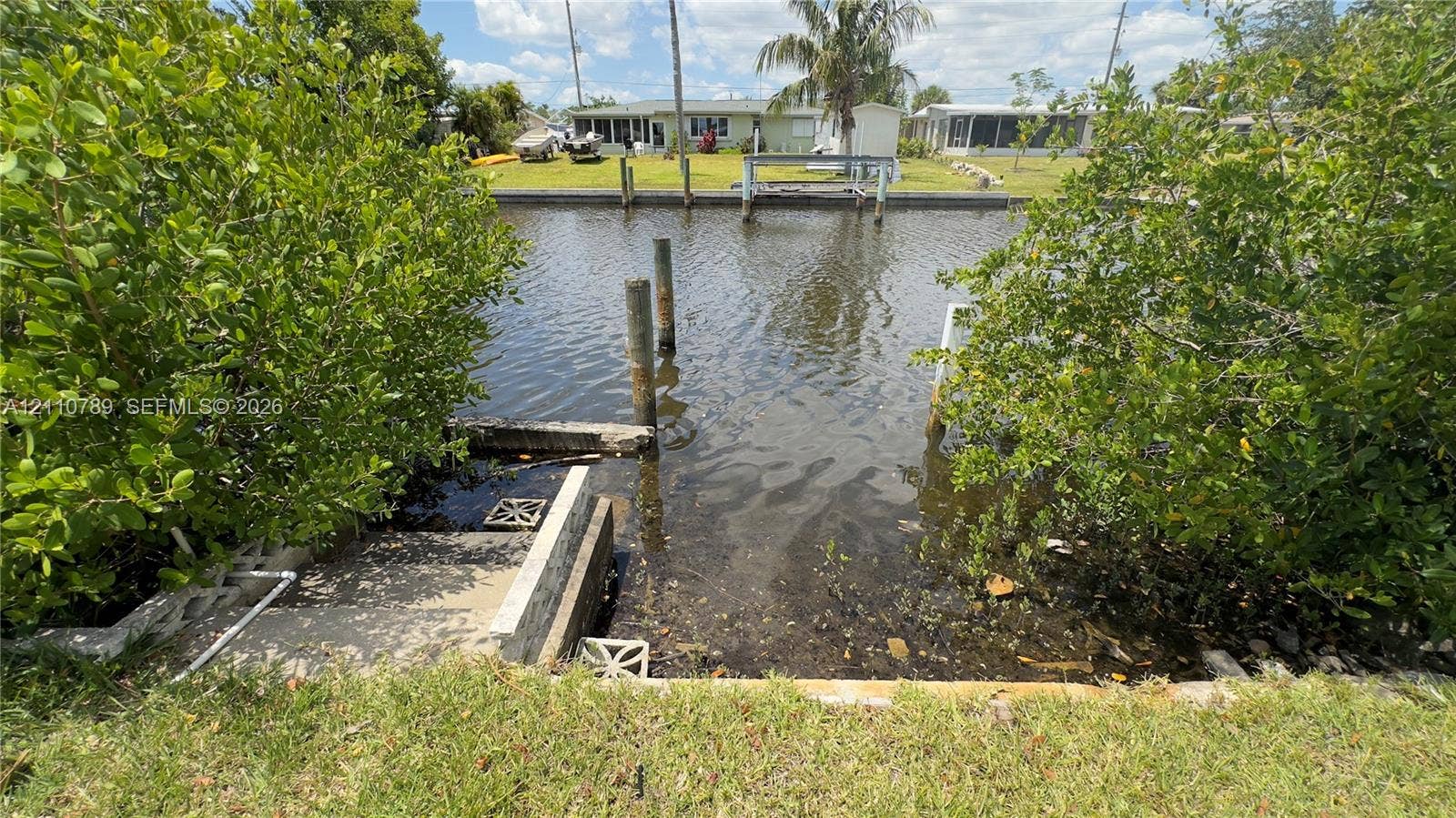 Canal-front property featuring a concrete bulkhead, private dock pilings, and stone stairs leading to the water