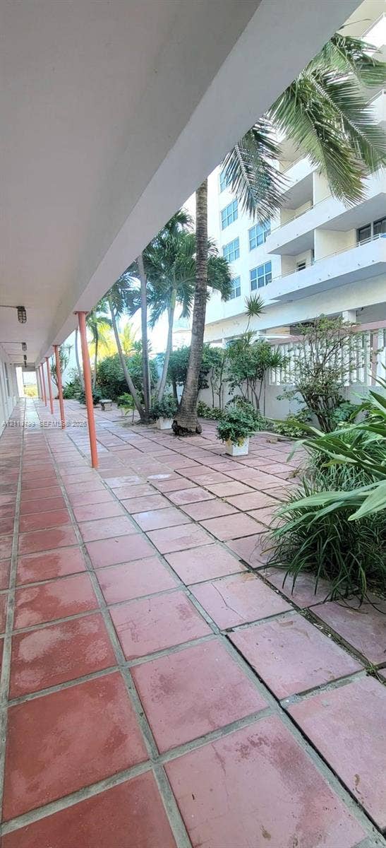Covered exterior walkway featuring terra cotta tile flooring, structural support columns, and mature palm landscaping