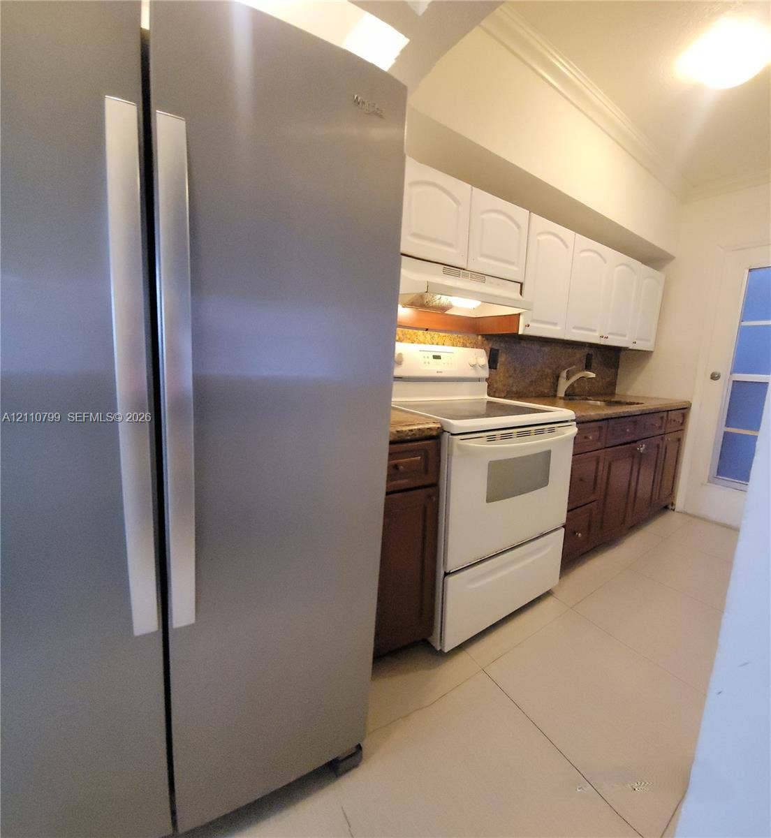 Kitchen featuring stainless steel side-by-side refrigerator, white appliance suite, dual-tone cabinetry, stone-finish countertops, and tile flooring