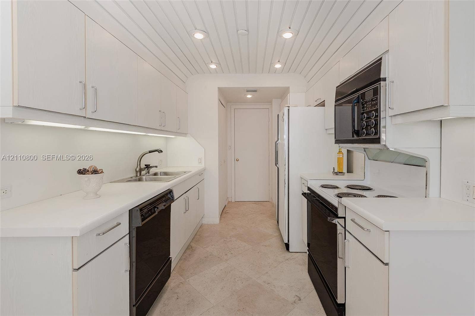 Galley kitchen featuring white cabinetry, under-cabinet lighting, a vertical-plank ceiling with recessed lighting, stone-tile flooring, and built-in appliances