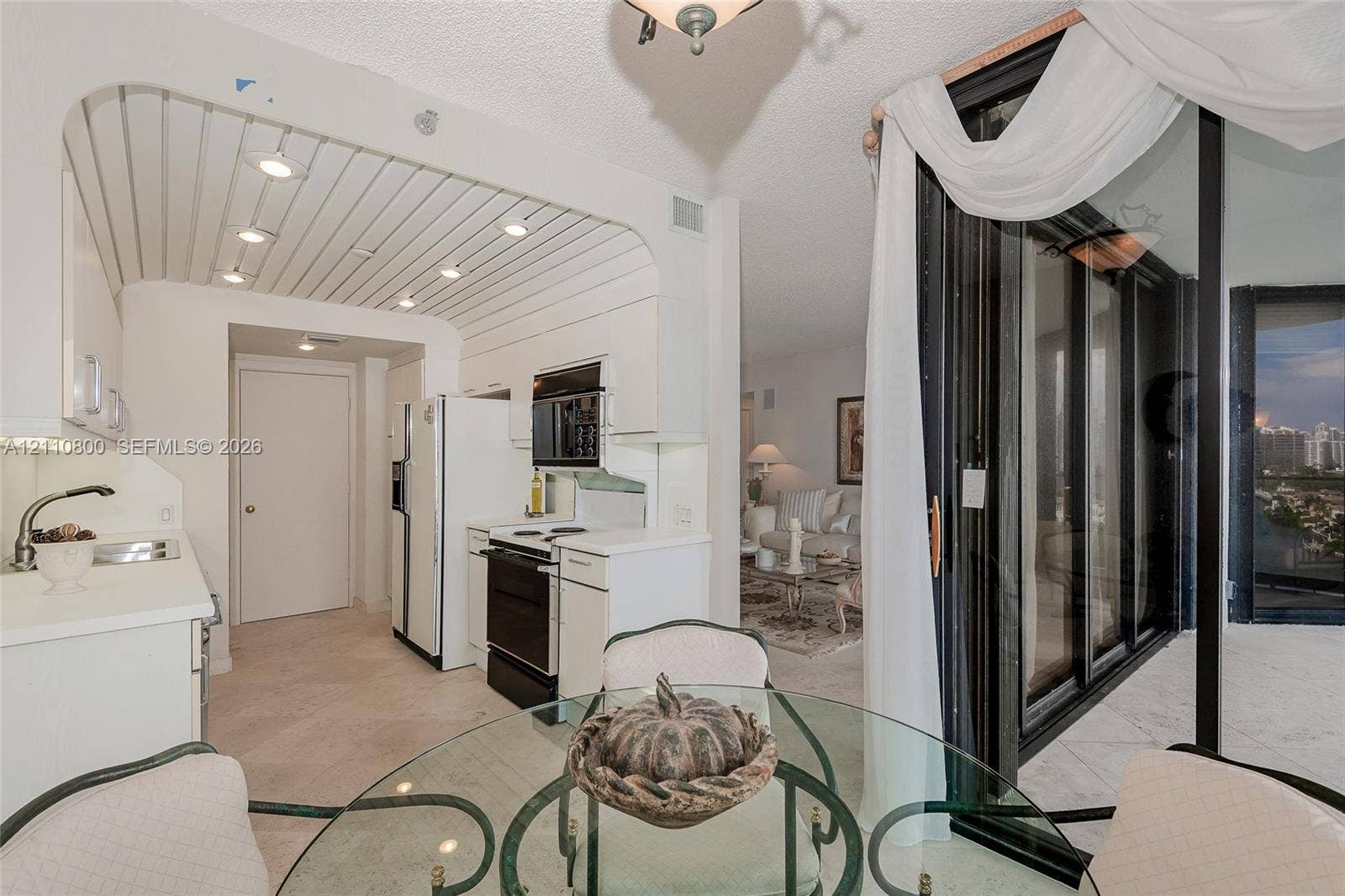 Kitchen featuring white cabinetry, solid-surface countertops, integrated cooktop, and an arched ceiling detail with recessed lighting, paired with floor-to-ceiling glass sliding doors