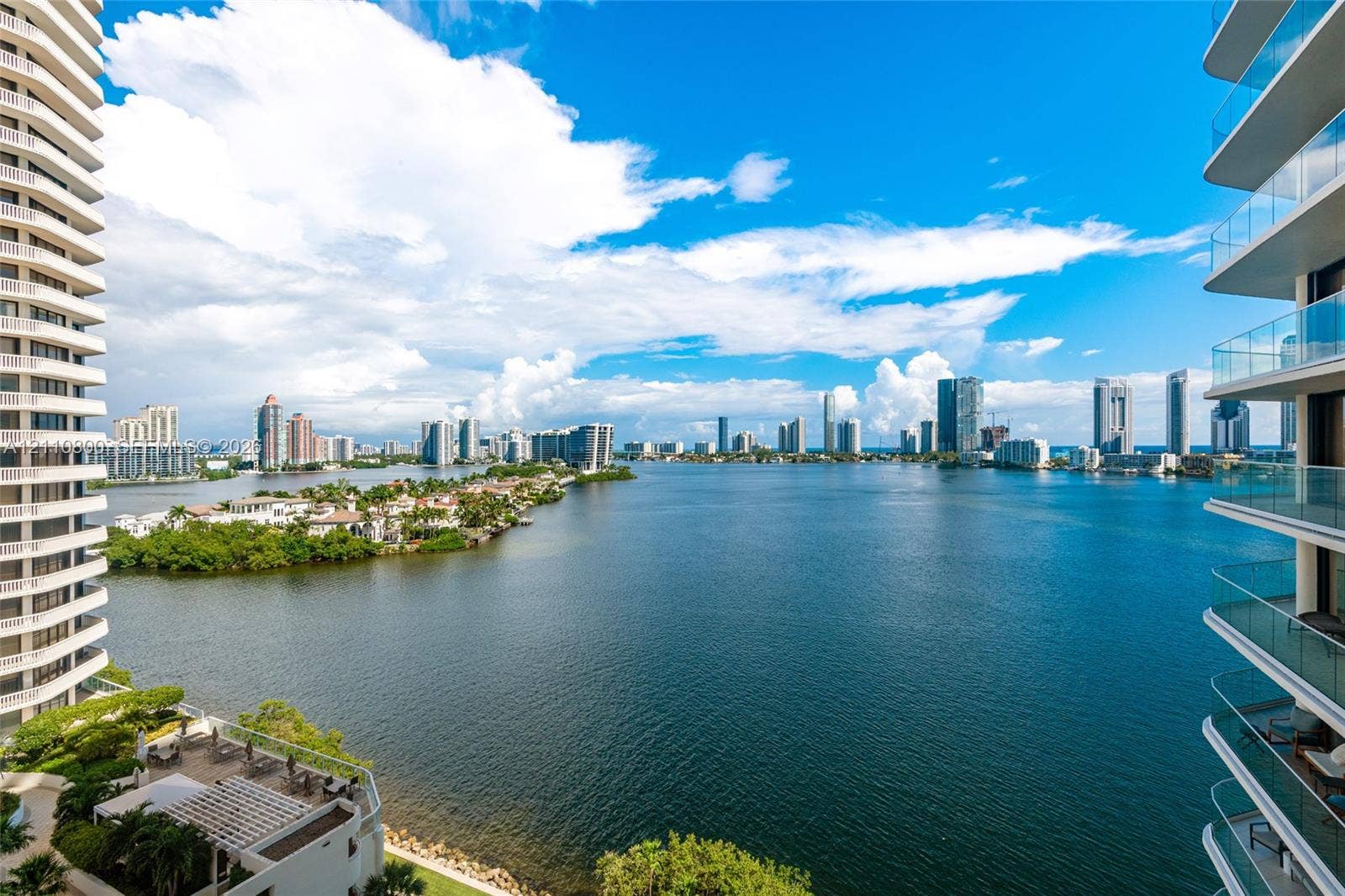 High-rise balconies featuring glass railings, overlooking a large body of water and a metropolitan skyline