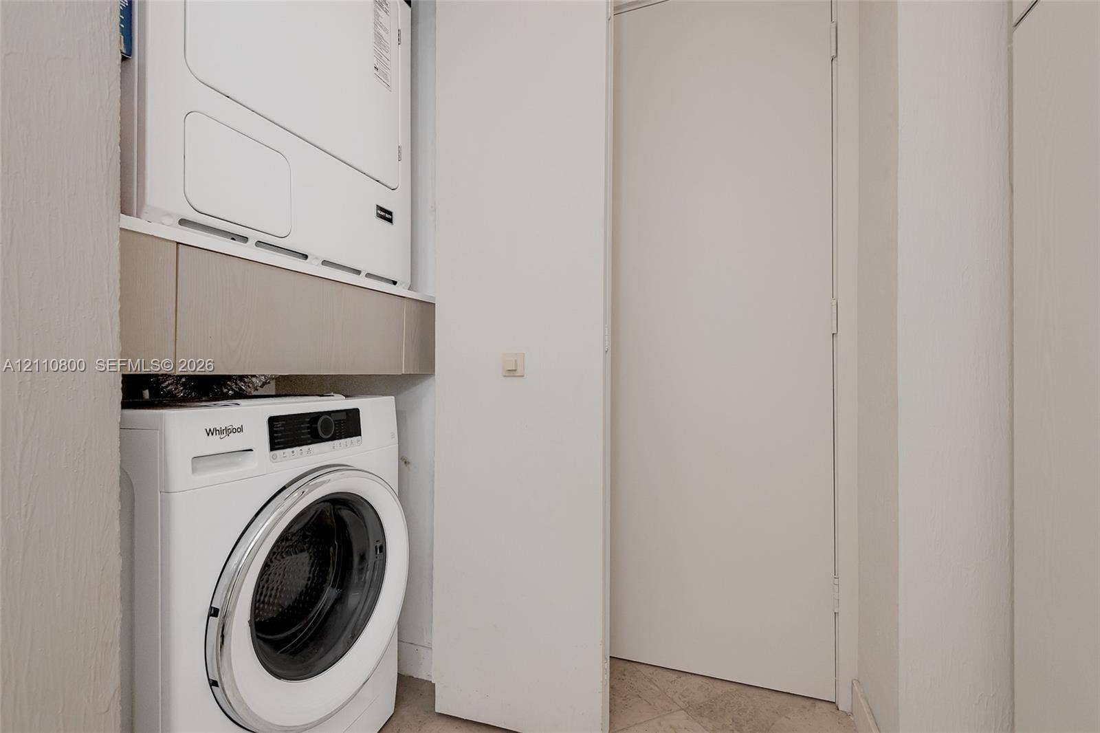 Laundry area featuring a stacked washer and dryer, integrated neutral-toned cabinetry, and tile flooring