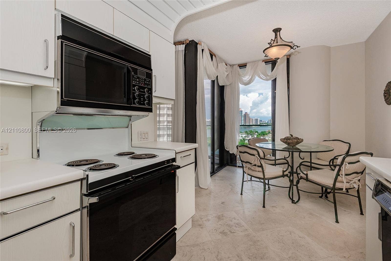 Kitchen featuring white cabinetry, integrated black appliances, stone-finish tile flooring, and floor-to-ceiling windows
