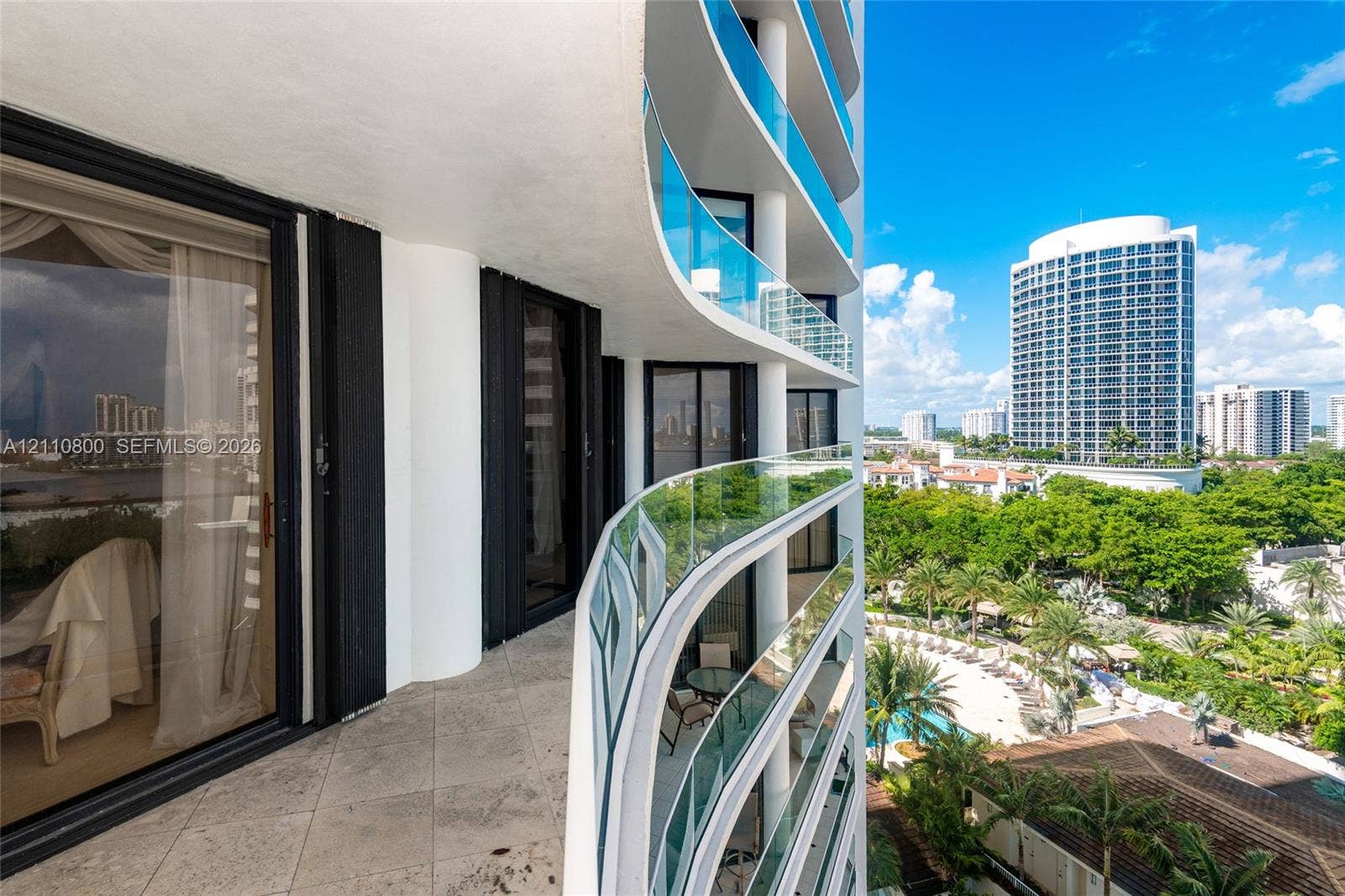 Curved private balcony with stone-tile flooring, glass panel railings, and floor-to-ceiling sliding glass doors
