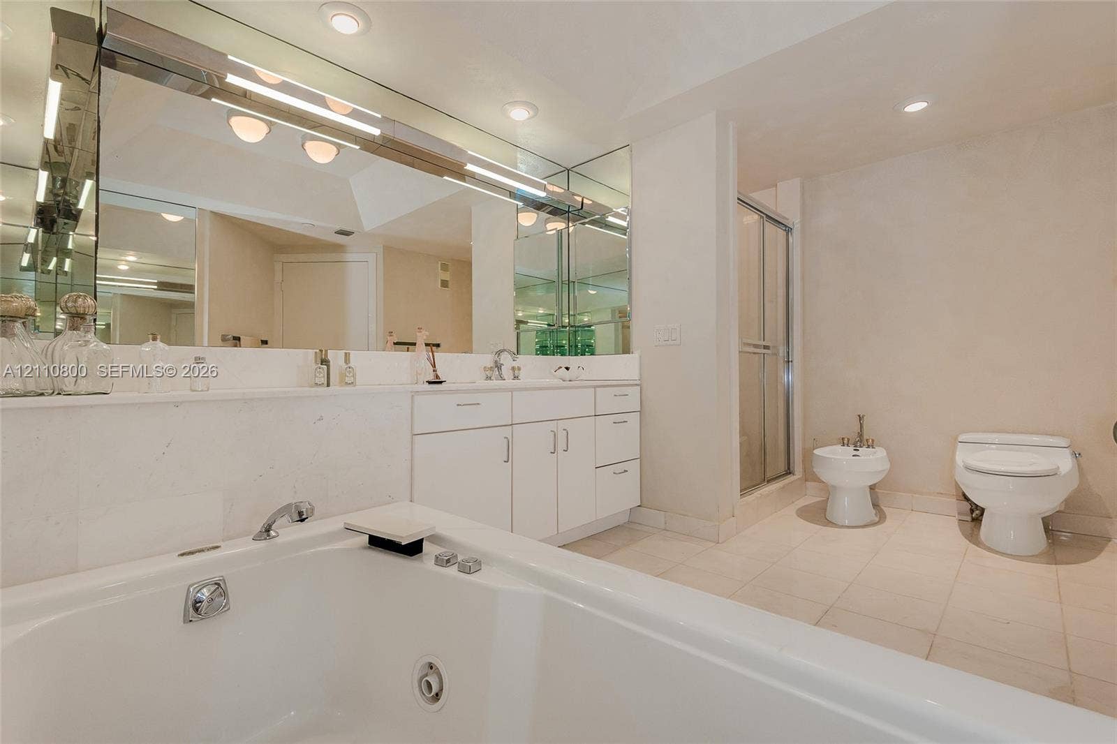 Bathroom featuring a soaking tub, expansive wall-to-wall mirror, white cabinetry with stone countertop, walk-in shower with glass enclosure, and tile flooring