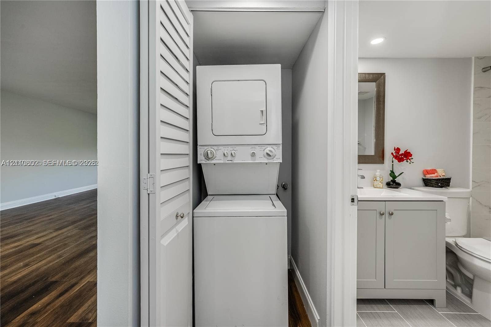Laundry closet featuring a white stacked washer and dryer unit behind louvered bi-fold doors, grey vanity cabinet with a white countertop, and tiled flooring