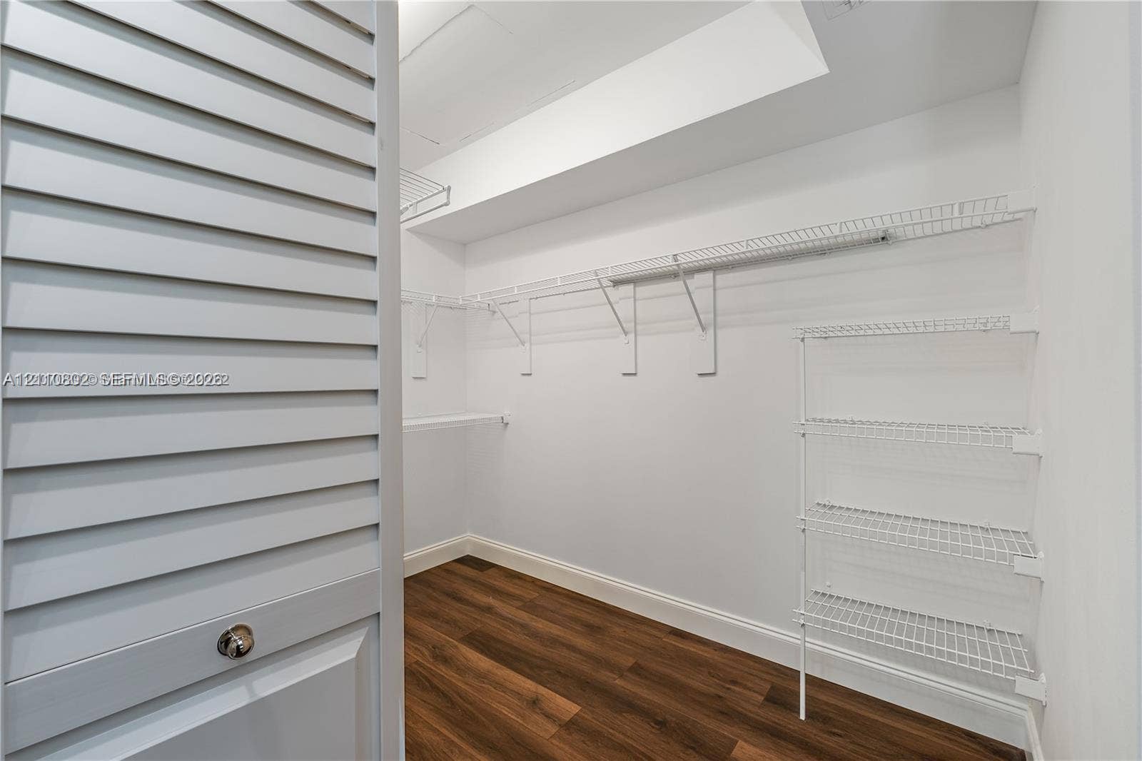 Walk-in storage space featuring wood-finish flooring, white louvered doors, and multi-tier wire shelving units