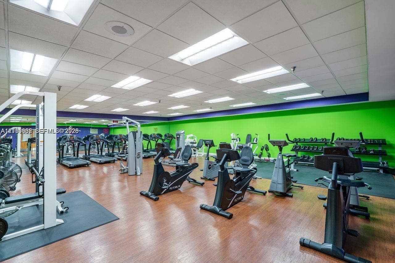 Fitness facility featuring wood-finish flooring, a suspended acoustic tile ceiling, recessed lighting, and rubber flooring sections