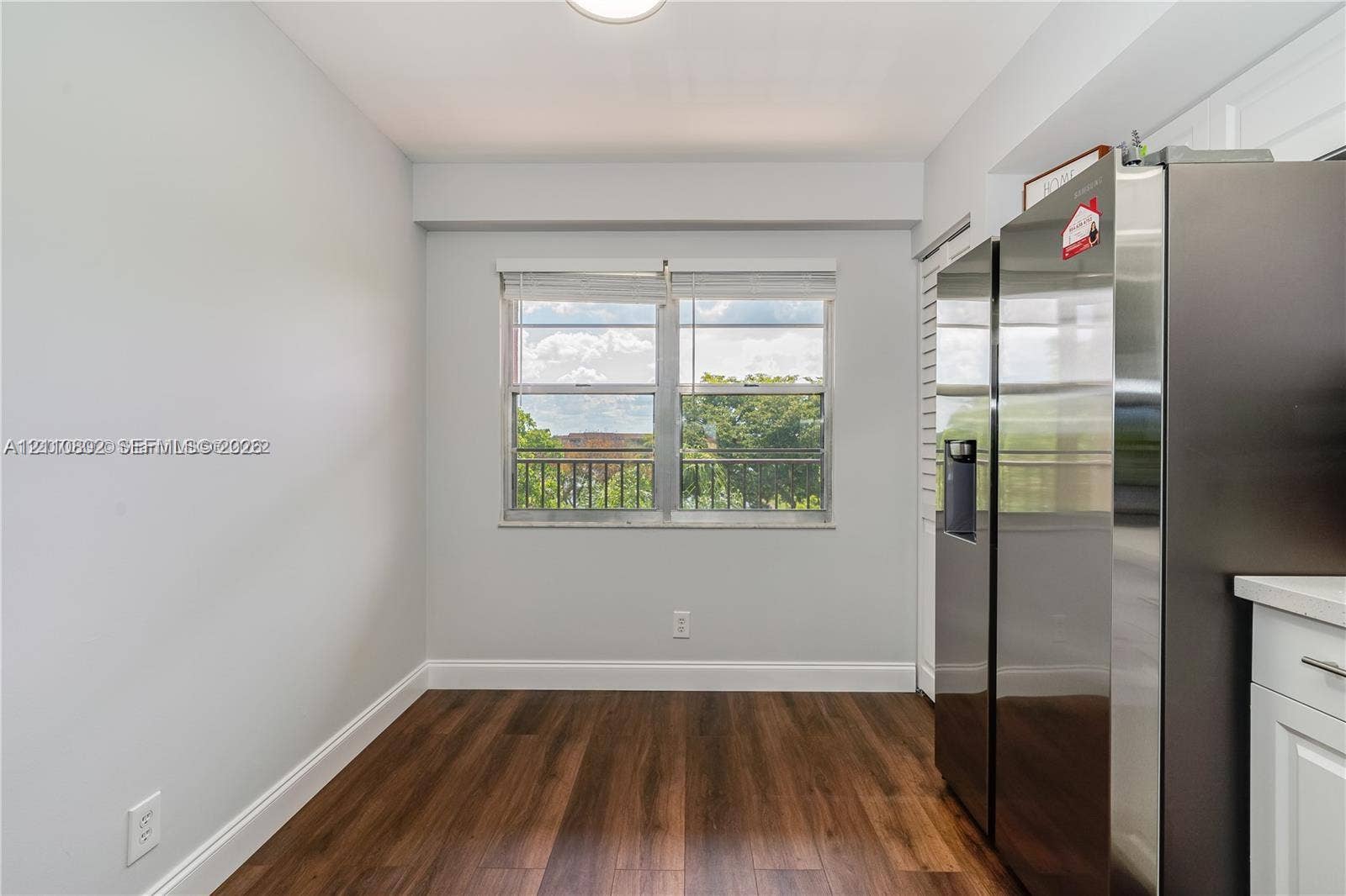 Wood-finish flooring, stainless steel side-by-side refrigerator, white shaker-style cabinetry, and horizontal sliding window with metal railing