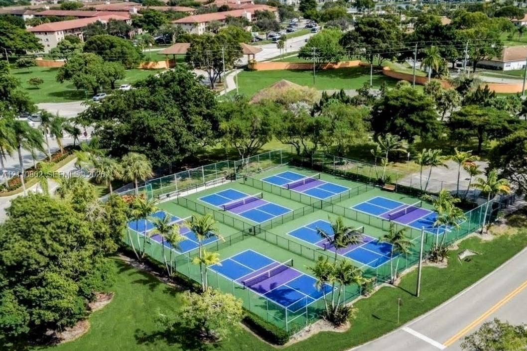 Multi-court complex featuring six fenced sport courts with blue and purple playing surfaces, surrounded by mature trees and manicured lawn