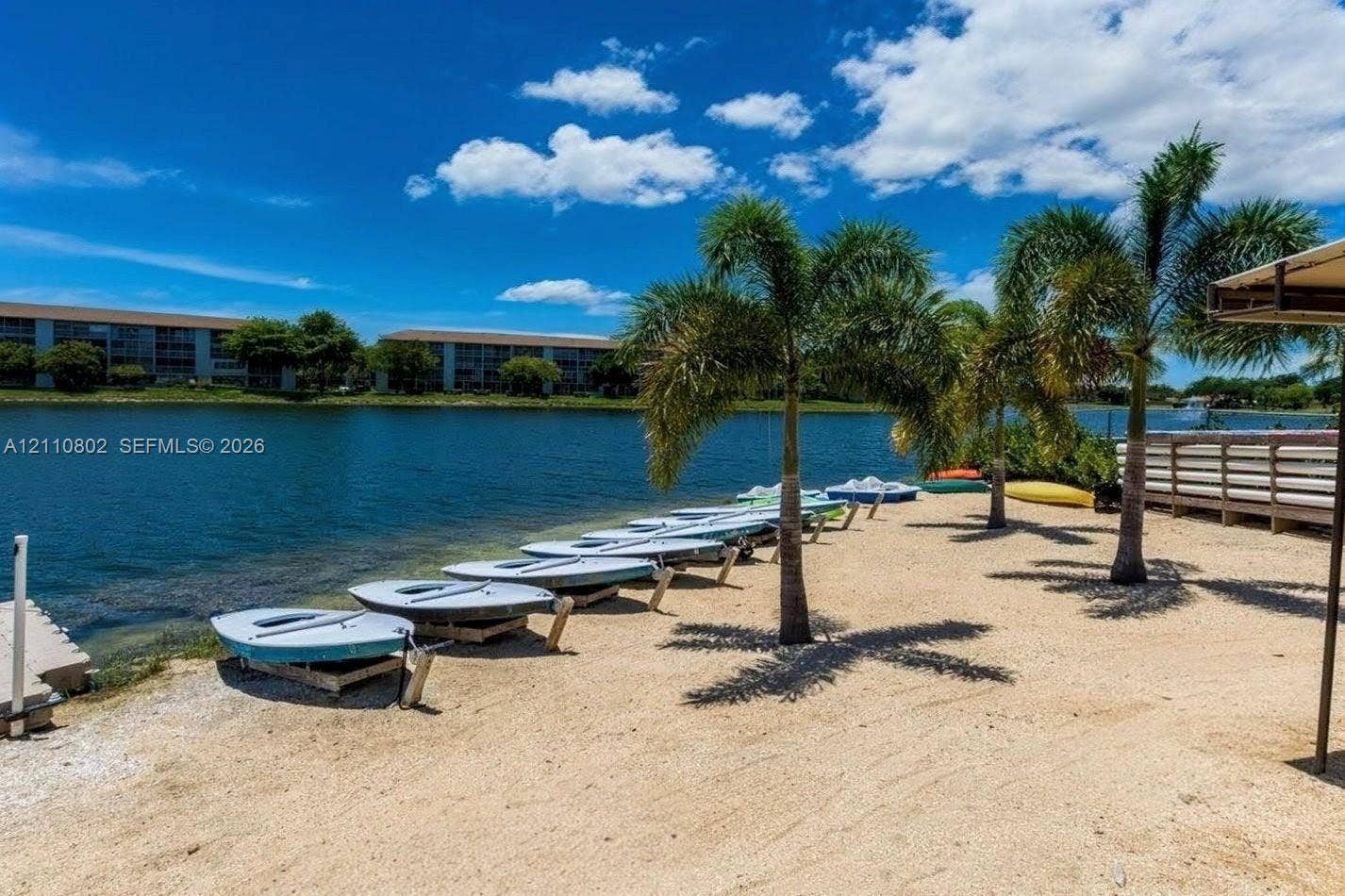 Waterfront access featuring a sandy beach, boat storage area, wooden bulkhead, and mature palm trees