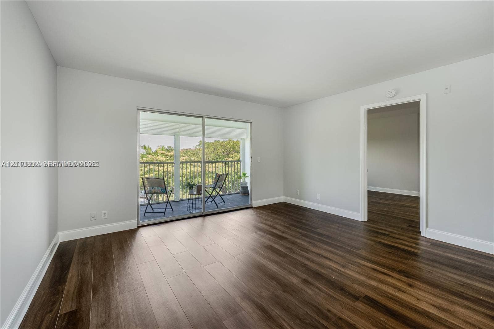 Interior room featuring wood-finish flooring, neutral wall tones, and sliding glass doors opening to an exterior balcony