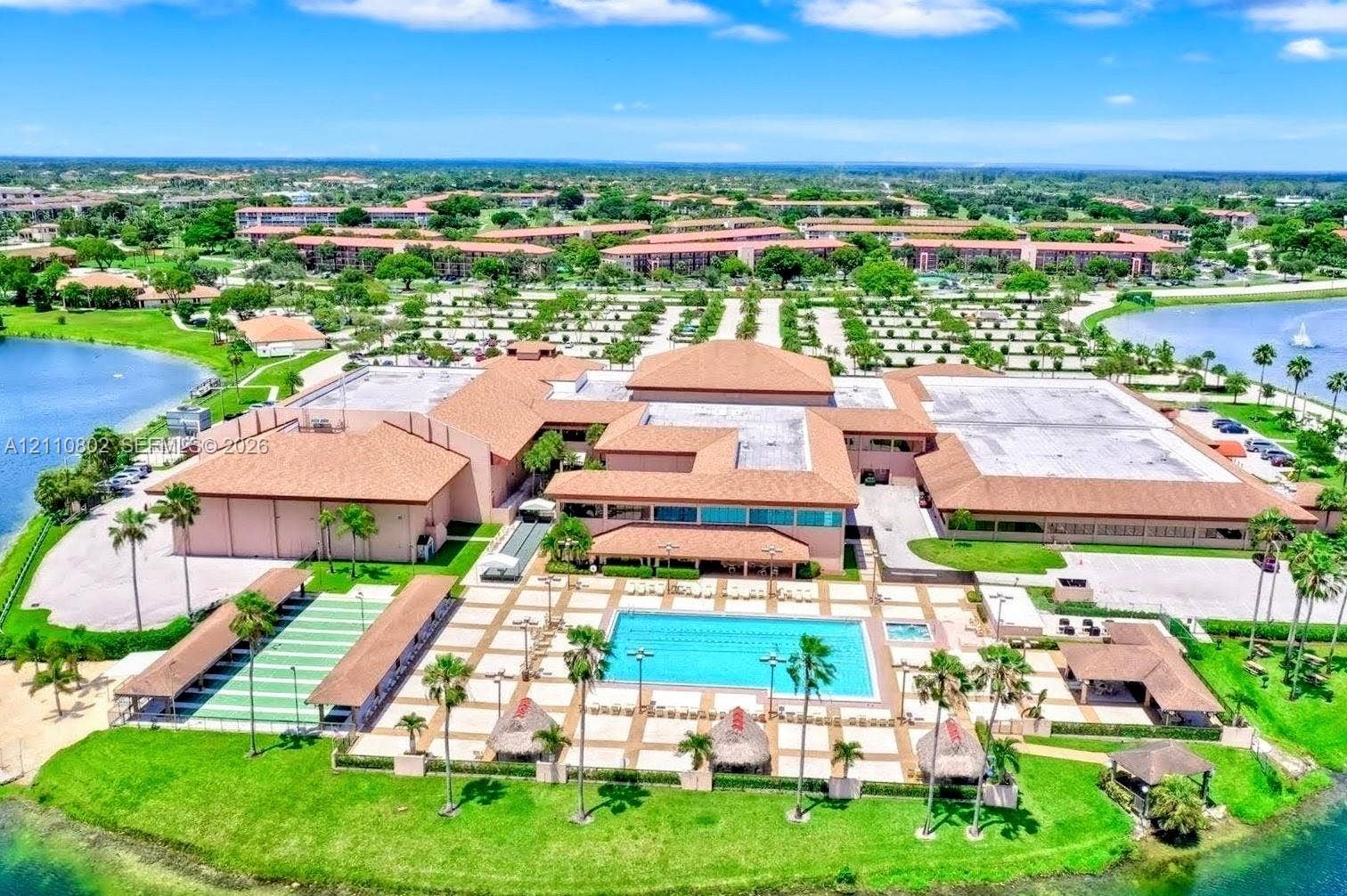 Large-scale commercial facility featuring a multi-section terracotta tile roof, expansive paved pool deck, rectangular swimming pool, and dedicated covered outdoor recreation areas situated on a waterfront lot